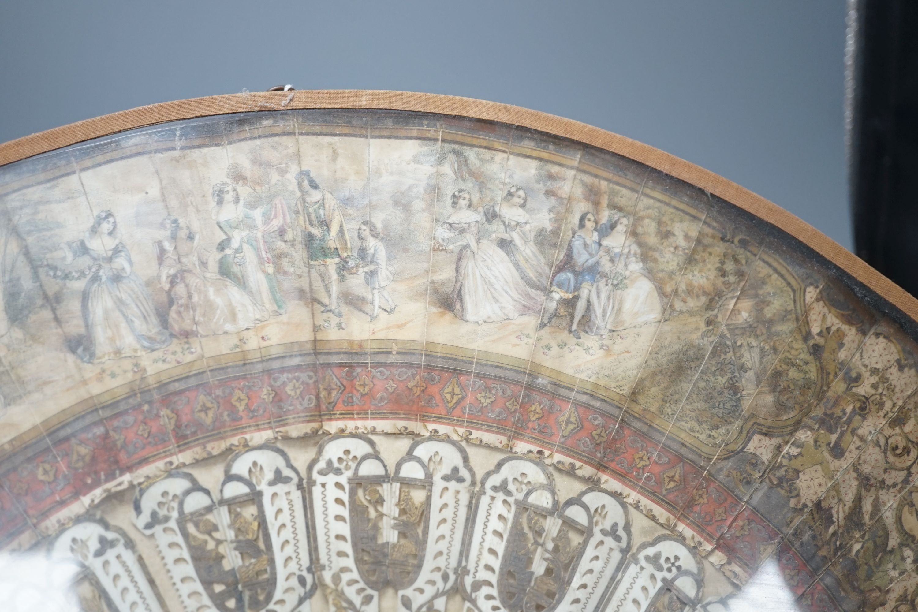 A cased 19th century French lithograph paper leaf and bone stick fan, 56 cms wide.